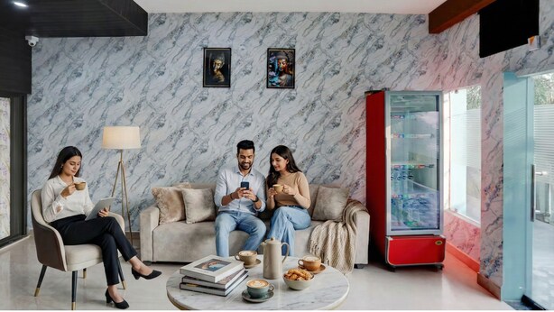 A modern living room with a marble-patterned wall, a red vending machine, and a coffee table with books and pastries. - Via Atithi Inn (Varanasi)