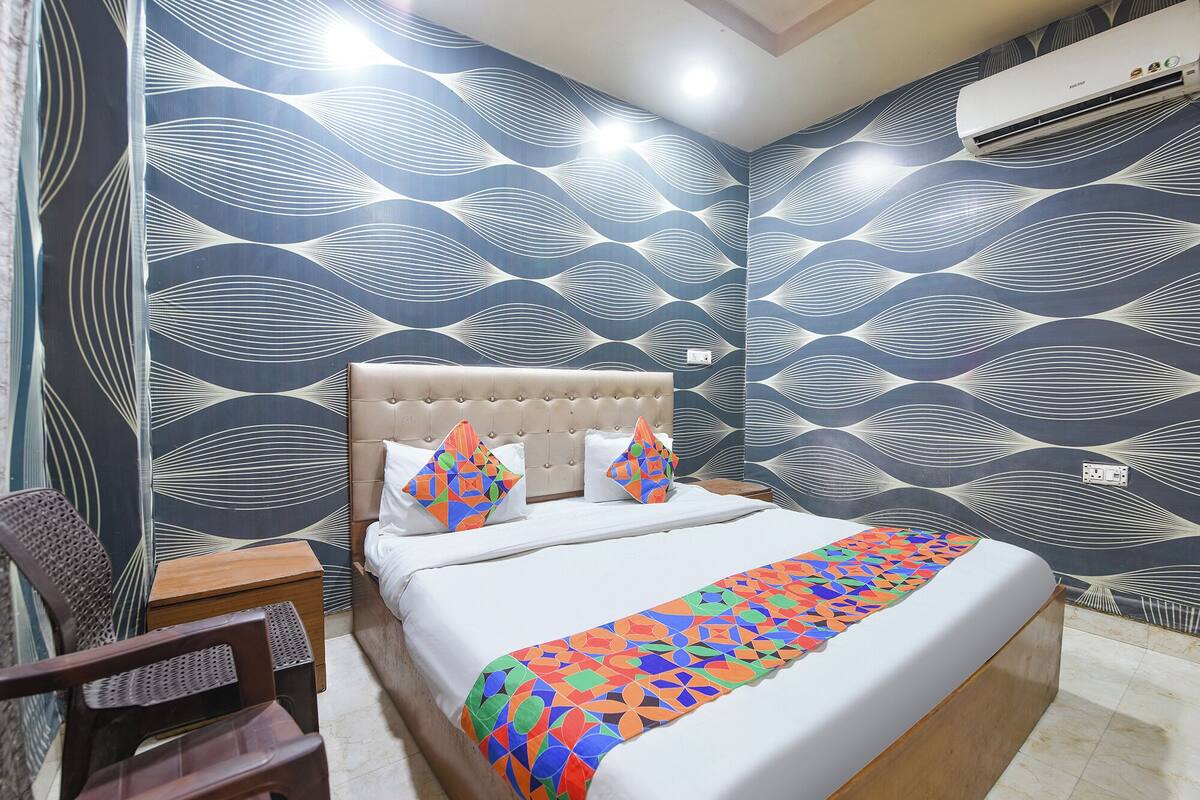 A bedroom with a tufted headboard, a bed with white bedding, colorful pillows, and a patterned wall.