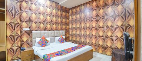 A bedroom with a patterned wallpaper, a bed with a colorful geometric throw, a bedside table, and a television.