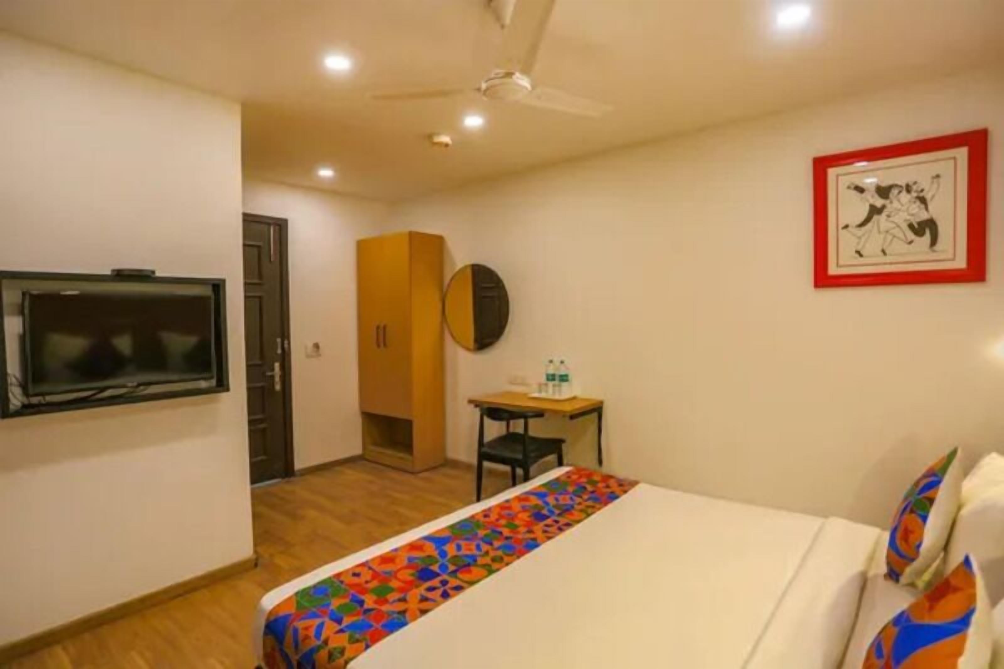 A hotel room with a bed, a TV, a wardrobe, a desk, and a framed picture on the wall.
