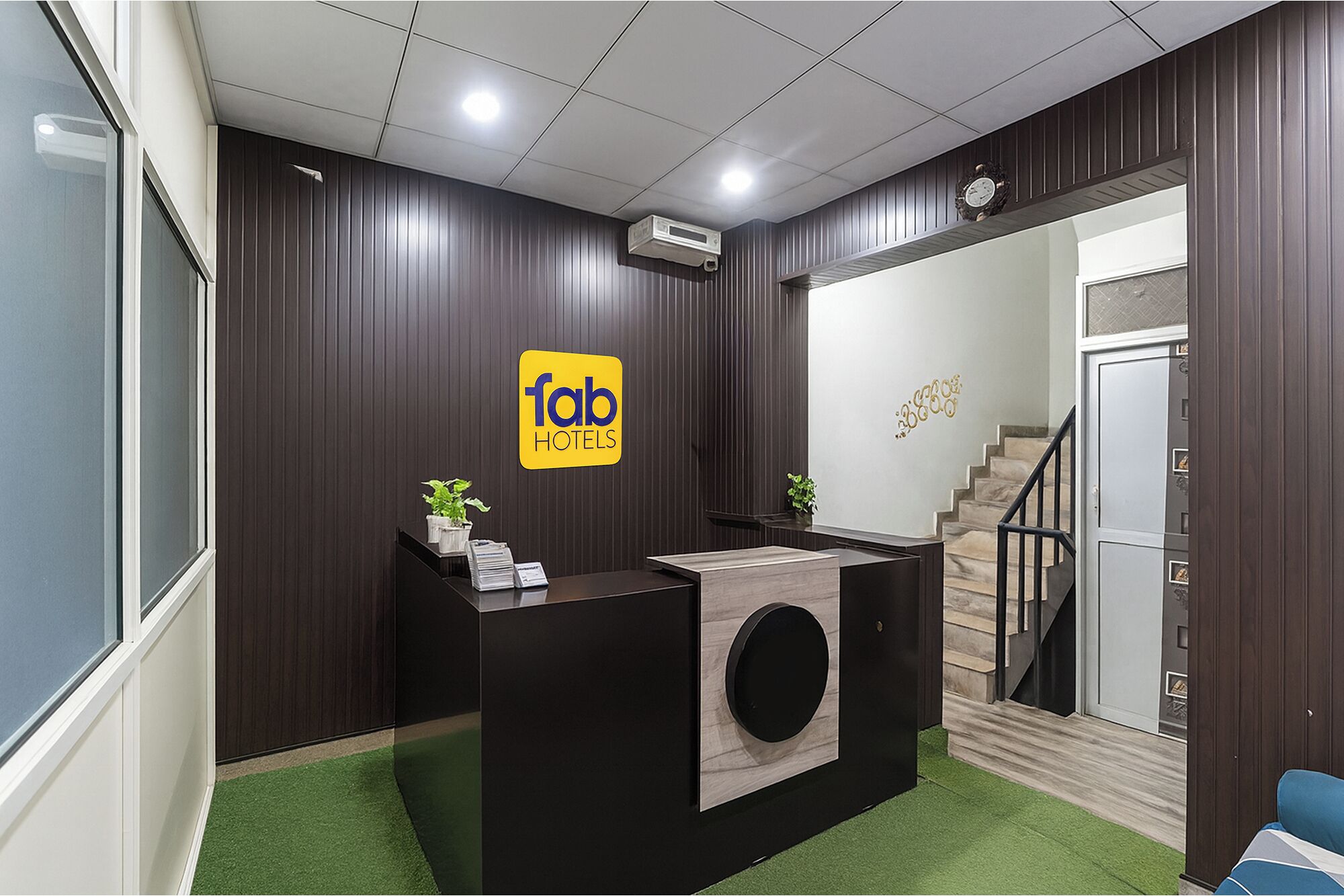 A reception area with a dark wood panel wall, a reception desk with a round black accent, and a staircase leading to an upper floor.