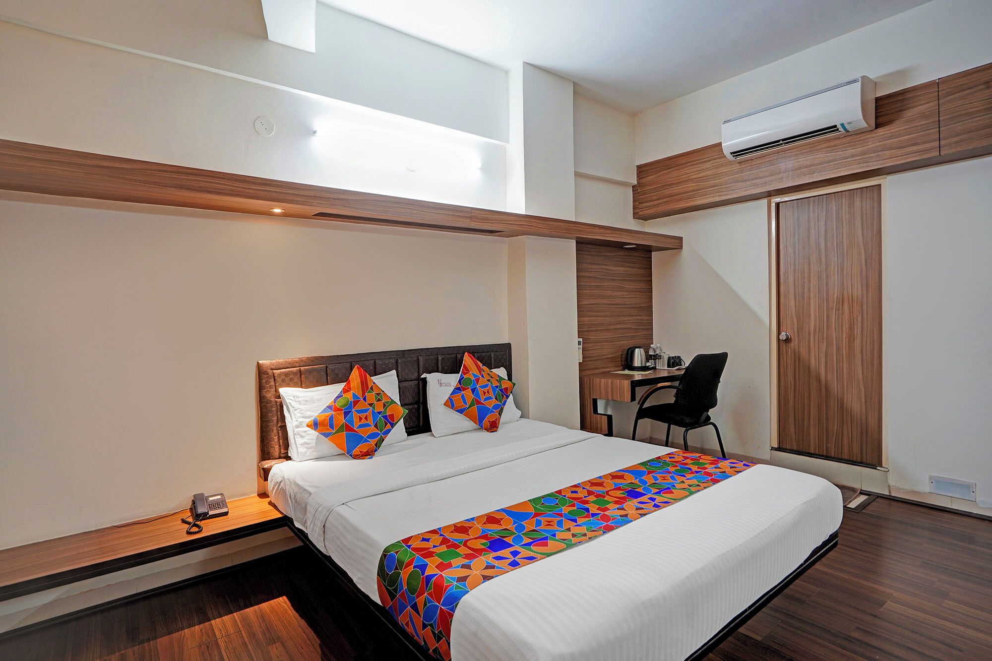 A modern hotel room with a large bed, a desk, and an air conditioning unit.