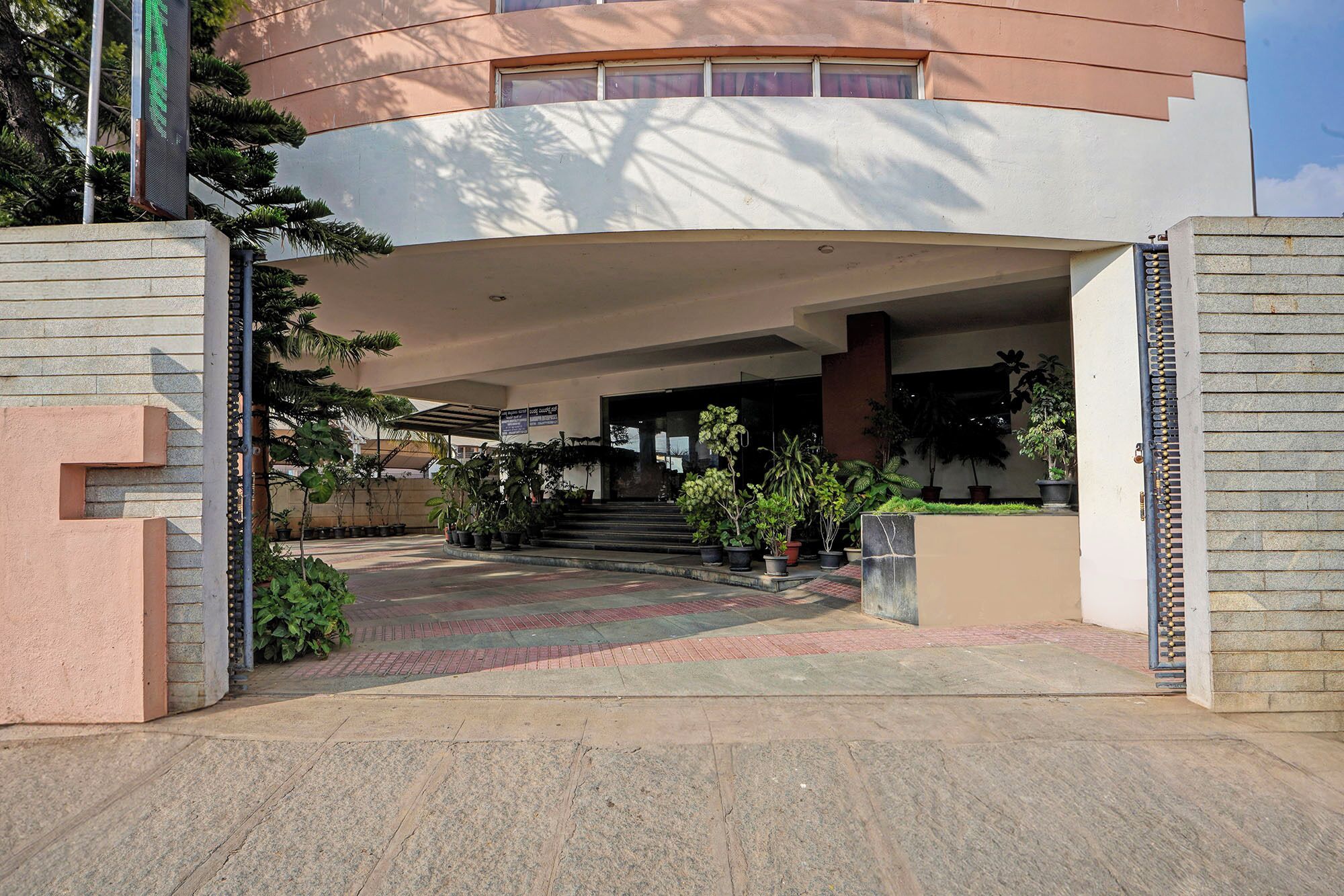 A modern building entrance with a curved facade, potted plants, and a clear sky.