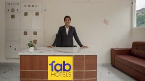 En hotellobby med en receptionsdisk där en receptionist sitter, en brun lädersoffa och en växt på disken.