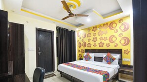 A hotel room with a bed, a nightstand, a chair, a ceiling fan, and a door. - Via BD Palace (New Delhi)