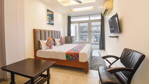 A modern hotel room with a bed, a desk, a chair, a ceiling fan, a TV, and a window with a city view. - Fabhotel 82 Inn (New Delhi)
