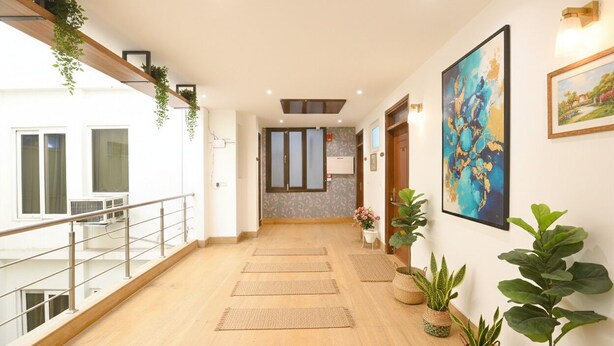 A hotel corridor with a wooden floor, a railing on the left, and potted plants along the right wall. - Fabhotel 82 Inn (New Delhi)