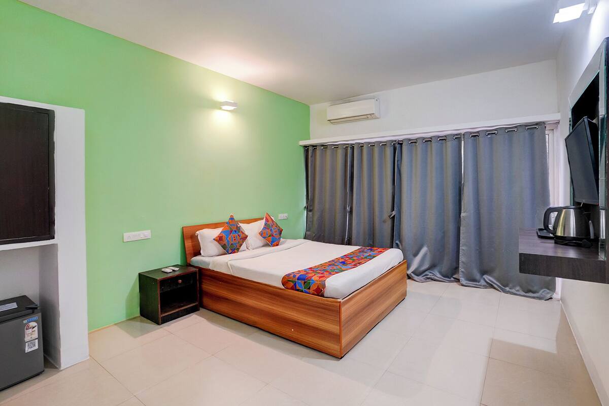 A bedroom with a bed, a nightstand, a TV, an air conditioner, and a window with curtains.