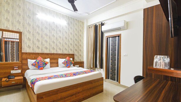 A hotel room with a wooden bed, a ceiling fan, an air conditioning unit, a wooden desk, and a window with curtains. - Fabhotel Divine (Gurugram)
