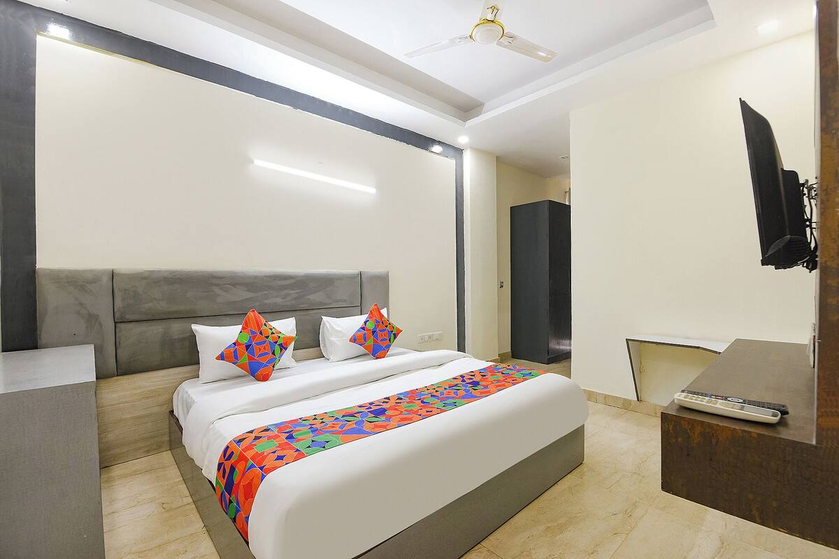 A modern hotel room with a large bed, a bedside table, a TV mounted on the wall, and a ceiling fan.