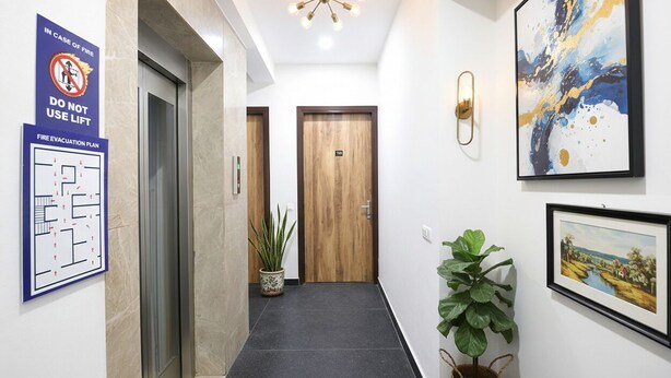 A hotel corridor with a fire evacuation plan, a lift, and a wooden door. - Fabhotel Ostan Stayz (Gurugram)