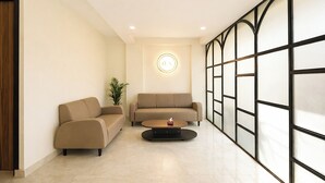 A modern living room with a sofa, a coffee table, and a decorative wall light. - Fabhotel Ostan Stayz (Gurugram)