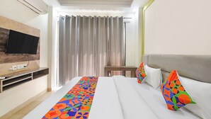 A hotel room with a bed, a TV mounted on the wall, a small table, and a window with curtains. - Fabhotel Ostan Stayz (Gurugram)