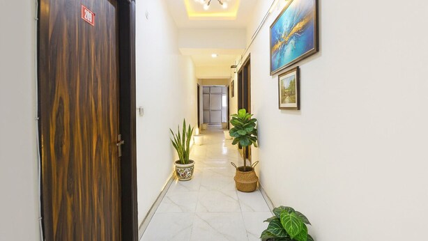 A hallway with a wooden door, potted plants, and framed artwork on the walls. - Via Town Plaza (New Delhi)