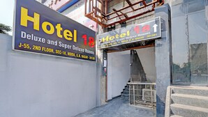 Hotellin sisäänkäynti, jossa on kyltit, joista käy ilmi, että toisessa kerroksessa sijaitsevat huoneet ovat Hotel 18 Deluxe- ja Super Deluxe -tyyppisiä. Osoite: G.B. Nagar, 201301.