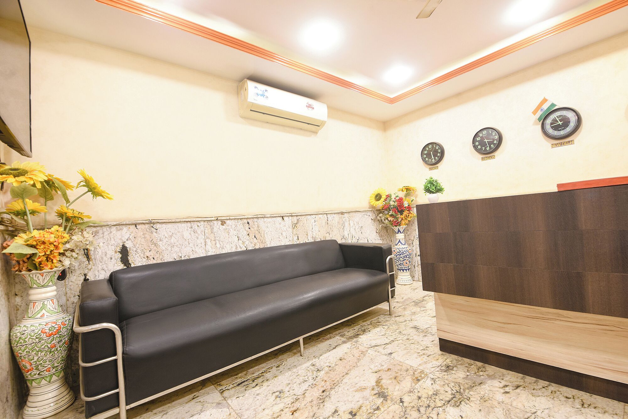 A reception area with a black sofa, a wooden reception desk, and three clocks indicating different cities.