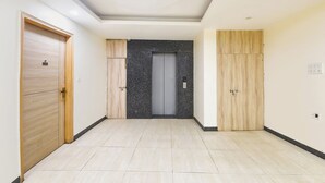 A hallway with a tiled floor, a grey elevator door, and wooden doors on either side. - Fabhotel Mahal (New Delhi)