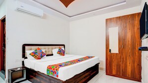 A bedroom with a bed, a wooden wardrobe, and an air conditioning unit. - Fabhotel Royal Garuda Palace (Ramanagara)