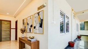 A modern hotel lobby with a wooden reception desk, abstract art on the wall, and potted plants. - Fabhotel Royal Garuda Palace (Ramanagara)