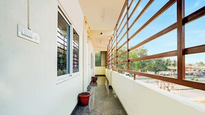 A corridor with large windows, potted plants, and a visible electrical outlet. - Fabhotel Royal Garuda Palace (Ramanagara)