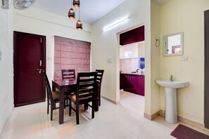 A dining area with a wooden table and chairs, a red door, and a kitchen visible through an open doorway. - Fabhotel Address 24 Suites (Bengaluru)