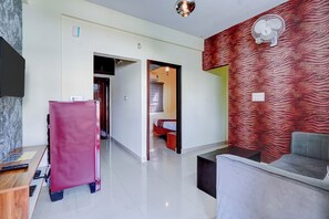 A hotel room with a modern design, featuring a large mirror, a red patterned wall, a seating area with a sofa and a small table, and a separate bedroom visible through an open door. - Fabhotel Address 24 Suites (Bengaluru)