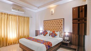 Quarto de hotel com uma cama grande, ar condicionado, mesa de cabeceira com abajur e guarda-roupa de madeira.