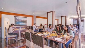 Um restaurante com mesas e cadeiras altas, uma pintura grande na parede e vista para um lago montanhoso.