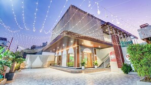 Un edificio moderno con una entrada destacada, rodeado por un jardín cuidado y luces colgantes.