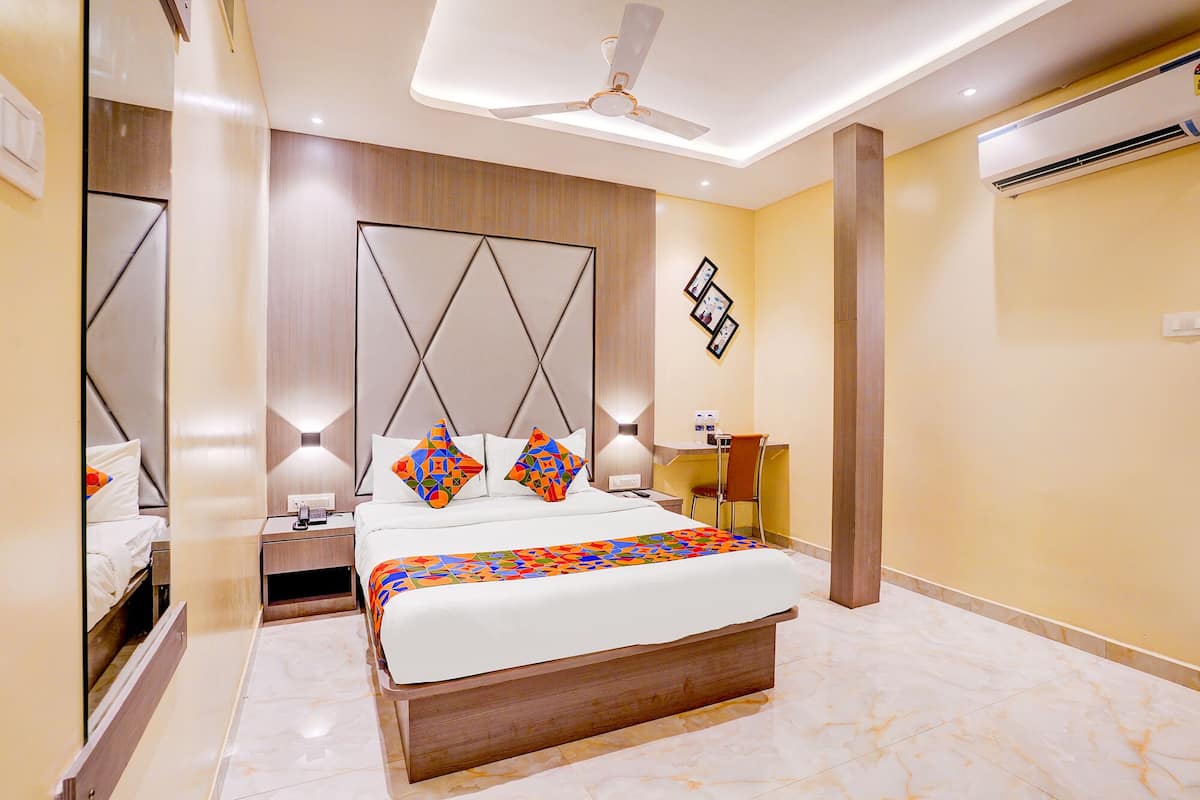 A modern hotel room with a large bed, bedside tables, a desk, and an air conditioning unit.