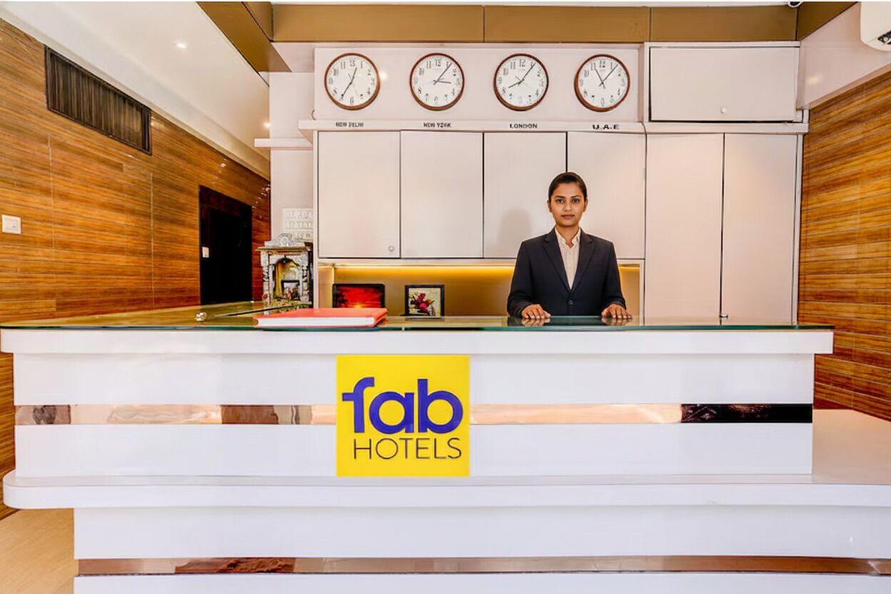 A hotel reception desk with clocks displaying different time zones, a receptionist, and a sign for 'fab hotels'.