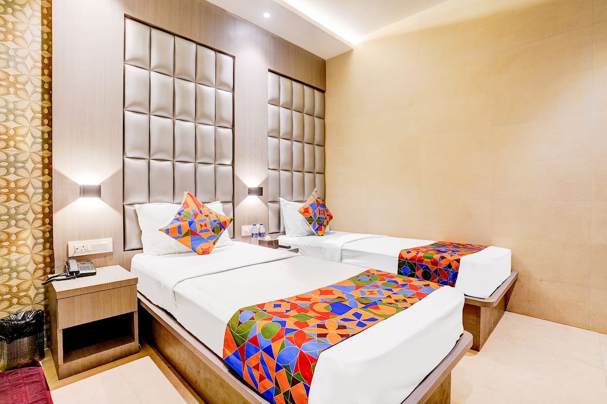 A hotel room with two beds, a wooden headboard, a bedside table with a phone, and a wall-mounted light.