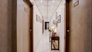 A hotel hallway with numbered doors, framed pictures on the walls, and a small table with a lamp and books. - Fabhotel Abrol Suites (Mumbai)