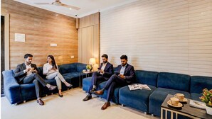 A modern lounge area with a blue sofa set, a ceiling fan, and a small table with a lamp and a magazine. - Fabhotel Abrol Suites (Mumbai)