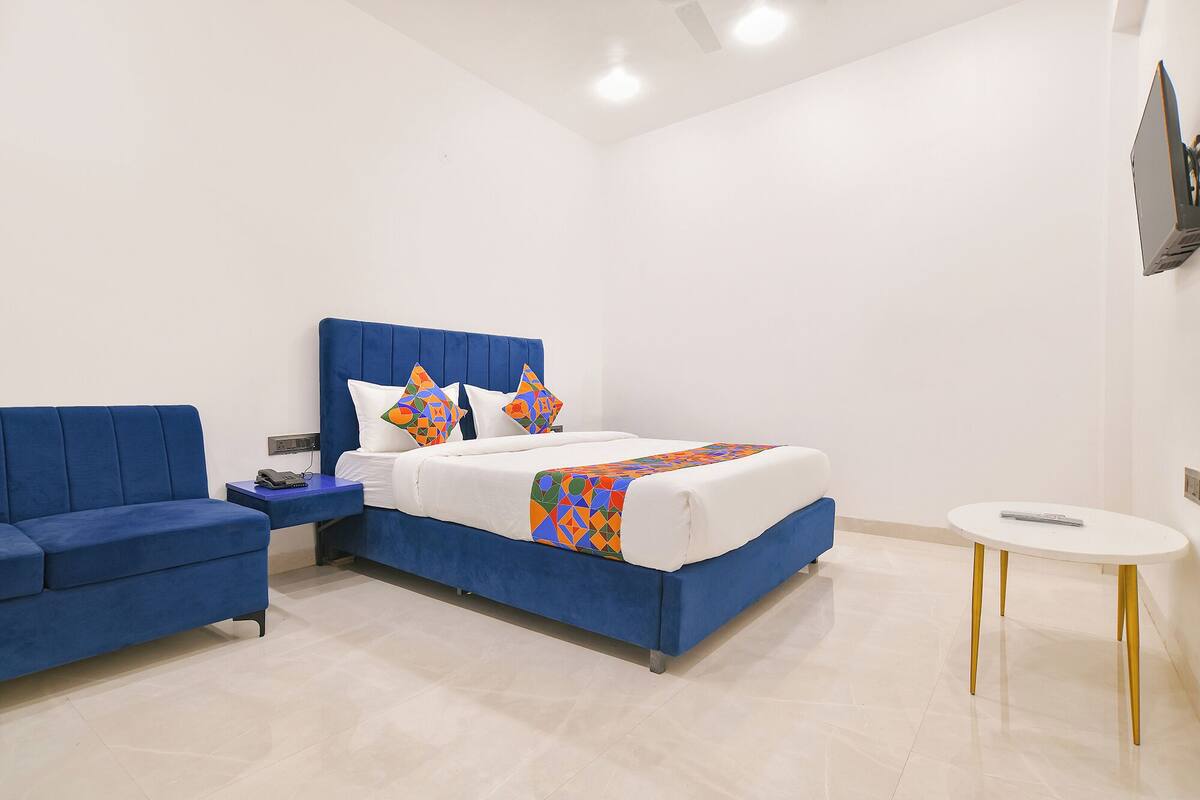 A modern bedroom with a blue sofa, a bed with colorful pillows, and a small white table.