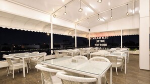 An outdoor dining area with white wicker furniture and glass tables, under a white canopy with string lights. - Fabhotel Blu Mark (Indore)