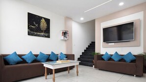 Un salon moderne avec deux canapés marron, une table basse en verre, un grand téléviseur à écran plat fixé au mur et un escalier menant à un autre niveau.