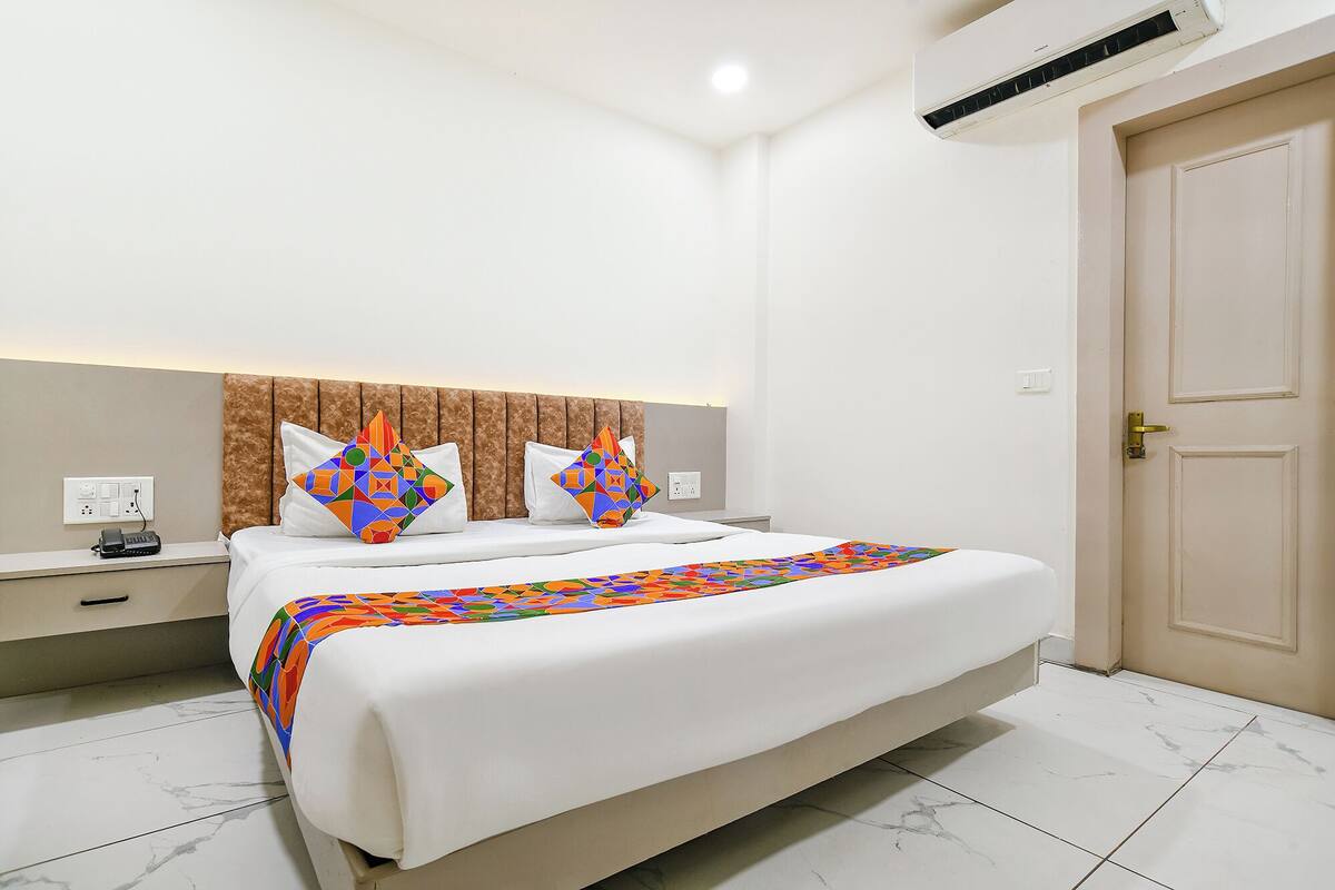 A hotel room with a large bed, a nightstand, a bedside table, a wall socket, and a door.