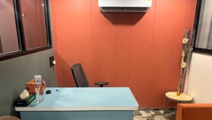 Quarto com escrivaninha azul, cadeira, mesa pequena e sofá.