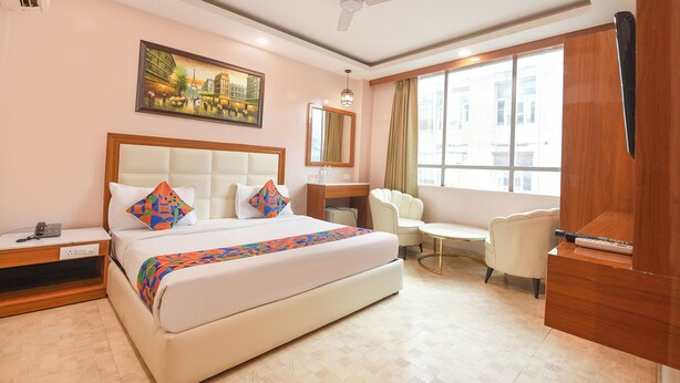 Une chambre d’hôtel avec un grand lit, un bureau, une chaise, un ventilateur de plafond, une fenêtre et un tableau au mur.