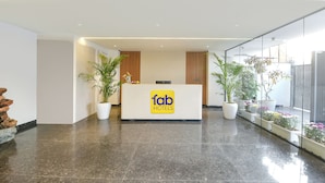 A hotel reception area with a modern design, featuring a reception desk, potted plants, and a glass wall providing a view of the outdoor area. - FabHotel Ivory Leaf- Nr Artemis Hospital Gurgaon (Gurugram)