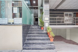 A staircase leading to a building entrance with a no smoking sign, a 2-time food menu sign, and potted plants. - Via Morning Glory (Bangalore)