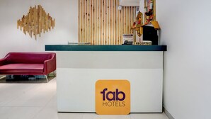 A reception area with a wooden slat wall, a reception desk, a red chair, and a sign for Fab Hotels. - Via Blissful Stays (Navi Mumbai)
