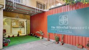 A hotel entrance with a red exterior wall, a sign advertising 'The Blissful Xiiere' with a logo, and a reception desk. - Via Blissful Stays (Navi Mumbai)