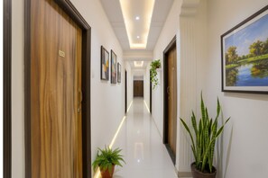 A hotel hallway with wooden doors, a polished floor, framed artwork, and potted plants. - Via Blissful Stays (Navi Mumbai)