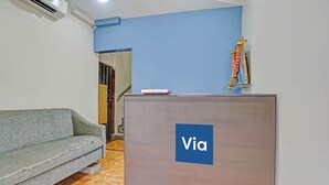 A reception desk with a 'Via' sign, a grey sofa, and a staircase in the background. - Via Stay Land (Mumbai)