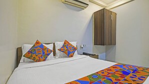 A hotel room with a bed, two pillows, a wooden wardrobe, and a patterned bedspread. - Via Stay Land (Mumbai)