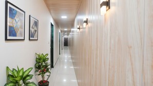A hallway with framed artwork on the walls, potted plants, and a wooden ceiling. - Via The Palace (Mumbai)