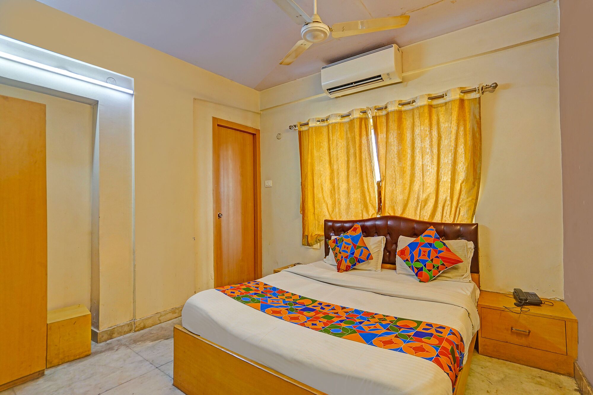 A bedroom with a bed, a bedside table, a nightstand, a ceiling fan, and an air conditioning unit.