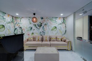 A modern living room with a beige sofa, a glass partition, and a floral wallpaper. - FabHotel Dharani Grand Madhapur - Image Gardens & Metro, Madhapur (Hyderabad)